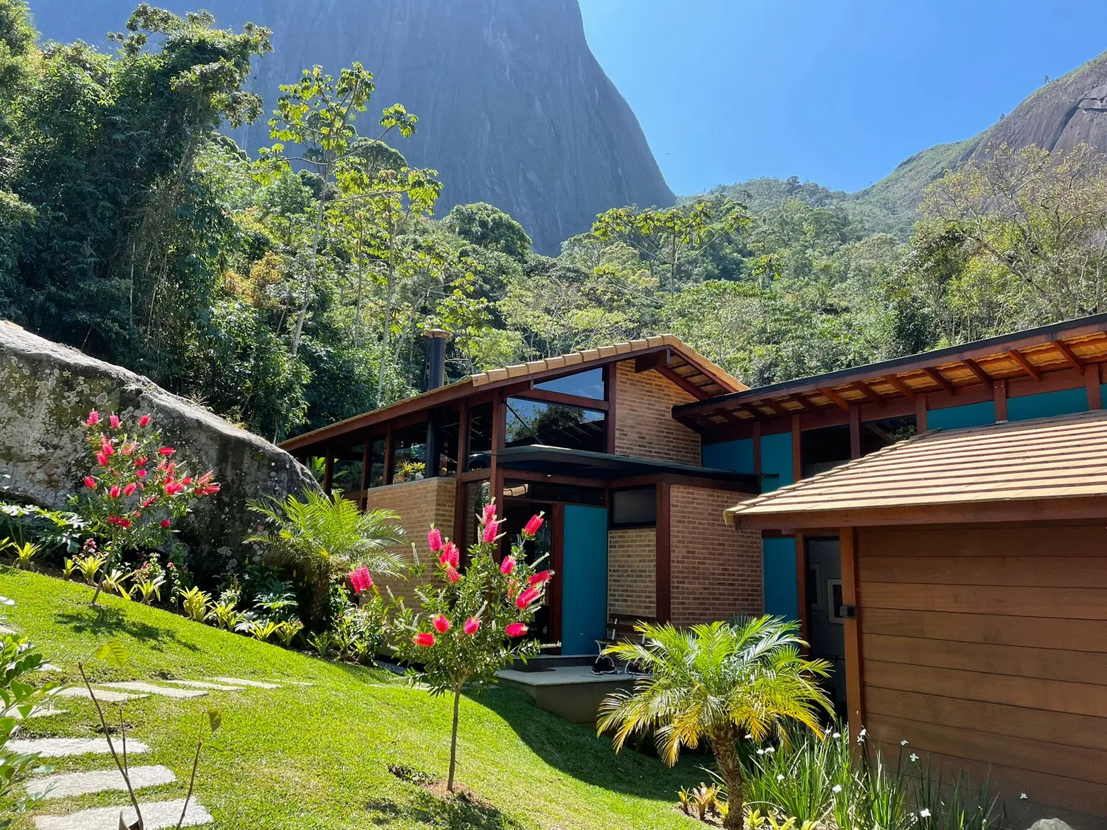Casa de madeira e alvenaria em jardim, com montanhas ao fundo